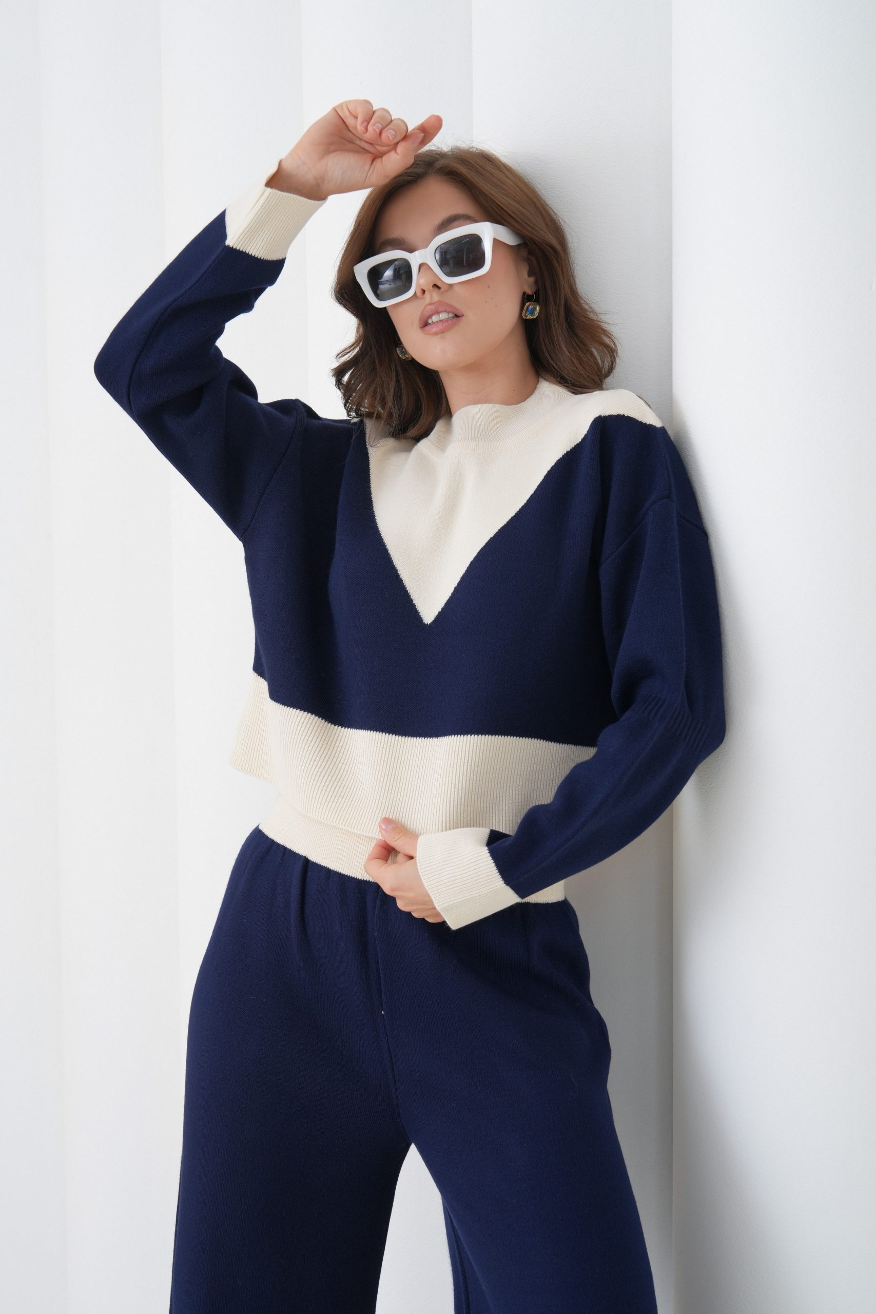 Lacivert ve krem renk bloklu Idole Woman triko takım giyen kadın model, beyaz duvar önünde poz veriyor.